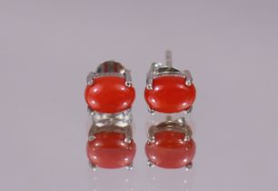 A pair of coral ear-studs, the oval cabochons set to un-marked white metal mounts. (1.8gm)