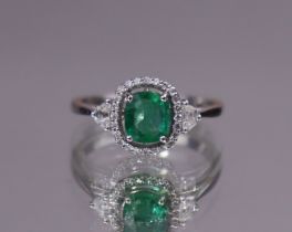 AN EMERALD & DIAMOND RING, the oval-cut emerald set within an open border of small round-cut