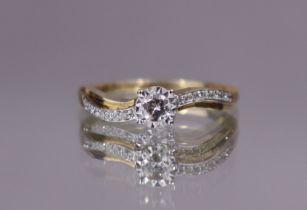 A diamond ring, the round brilliant-cut centre stone between waved shoulders set smaller diamonds,