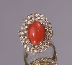 A diamond & coral ring, the central oval coral cabochon set within a double border of small round-