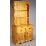 A pine small dresser the upper part with two open shelves & having a panelled base, the base