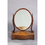 A Georgian mahogany oval swing dressing mirror on shaped supports & serpentine-front box base fitted