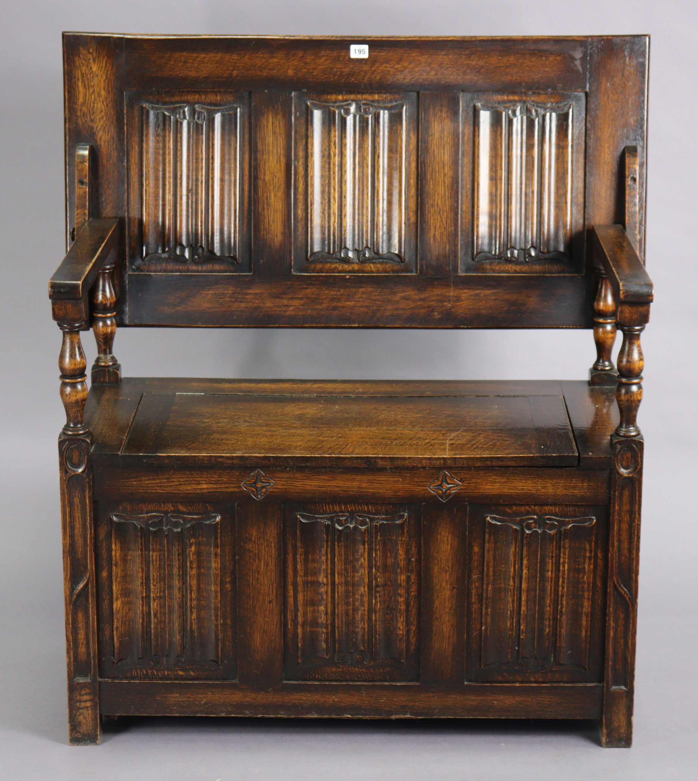 A reproduction oak monk’s bench with fold-over top, hinged box-seat, & carved linen-fold panels to