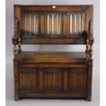 A reproduction oak monk’s bench with fold-over top, hinged box-seat, & carved linen-fold panels to