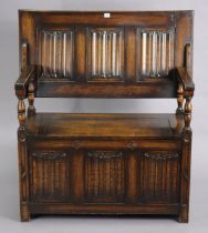 A reproduction oak monk’s bench with fold-over top, hinged box-seat, & carved linen-fold panels to