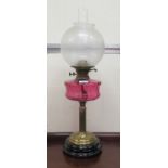 A late Victorian oil lamp with a cranberry glass reservoir, over a brass column and black china