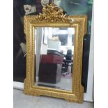 A late Victorian mirror with a bevelled plate, set in an ornate gilt gesso frame, surmounted by