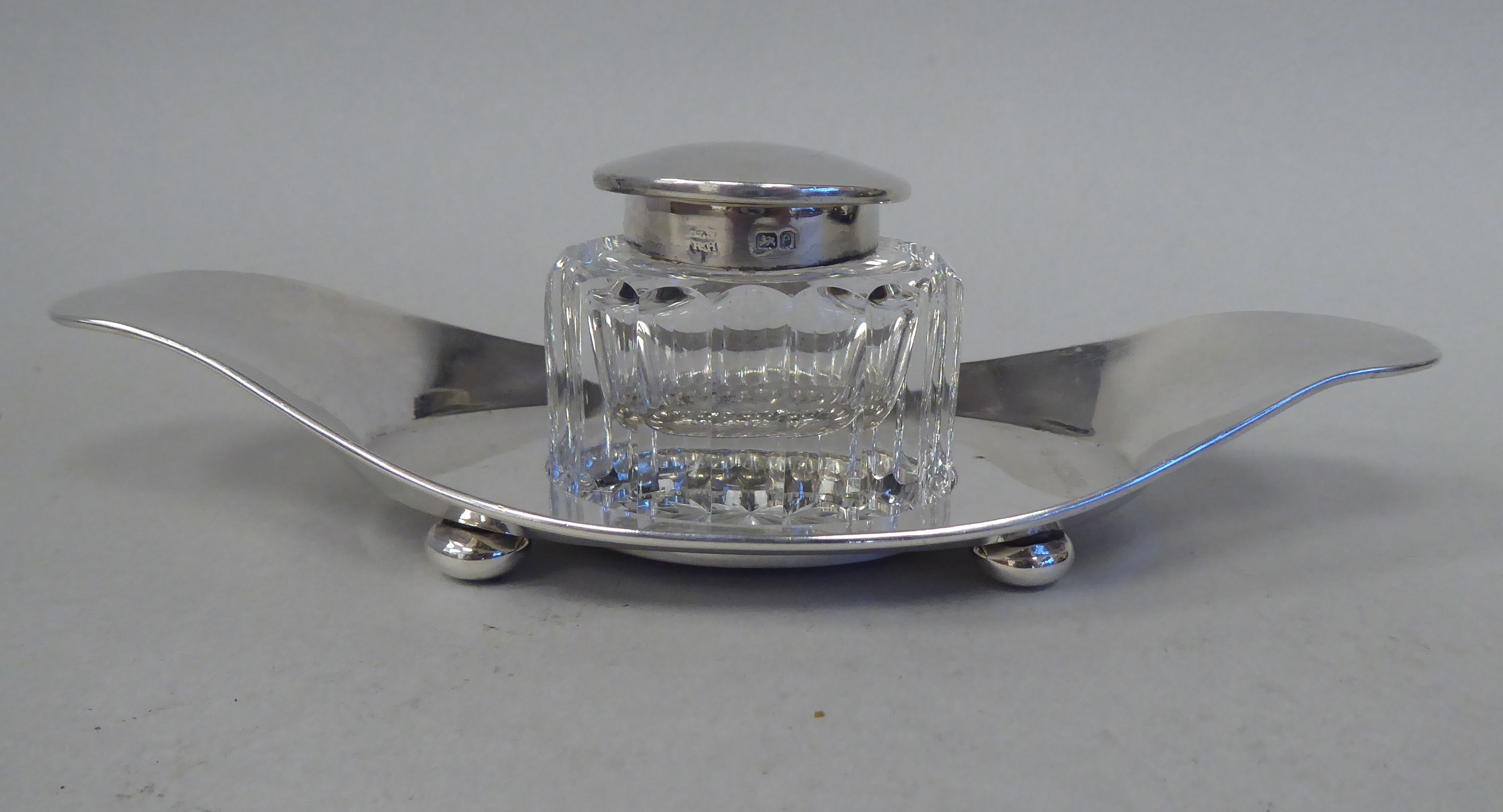 An Edwardian silver inkstand of oval tray design, on bun feet with a facet cut glass reservoir,