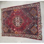 A Persian rug, decorated with a central motif, bordered by stylised designs, on a red ground  48"