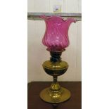 An early 20thC oil lamp, the brass reservoir on an integral stand  13"h with a cranberry coloured,