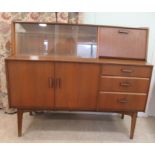 A 1960s teak finished sideboard, comprising an arrangement of fall flaps, sliding doors, drawers and