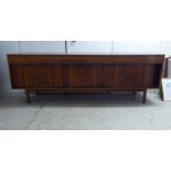 A 1970s rosewood sideboard with three frieze drawers, over three sliding doors, raised on turned