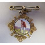 An engraved and shaped yellow metal medallion on a pin brooch, set with a coloured enamel tablet,
