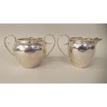 A silver cream jug of baluster form with a bead border, scrolled wire handle and a matching twin
