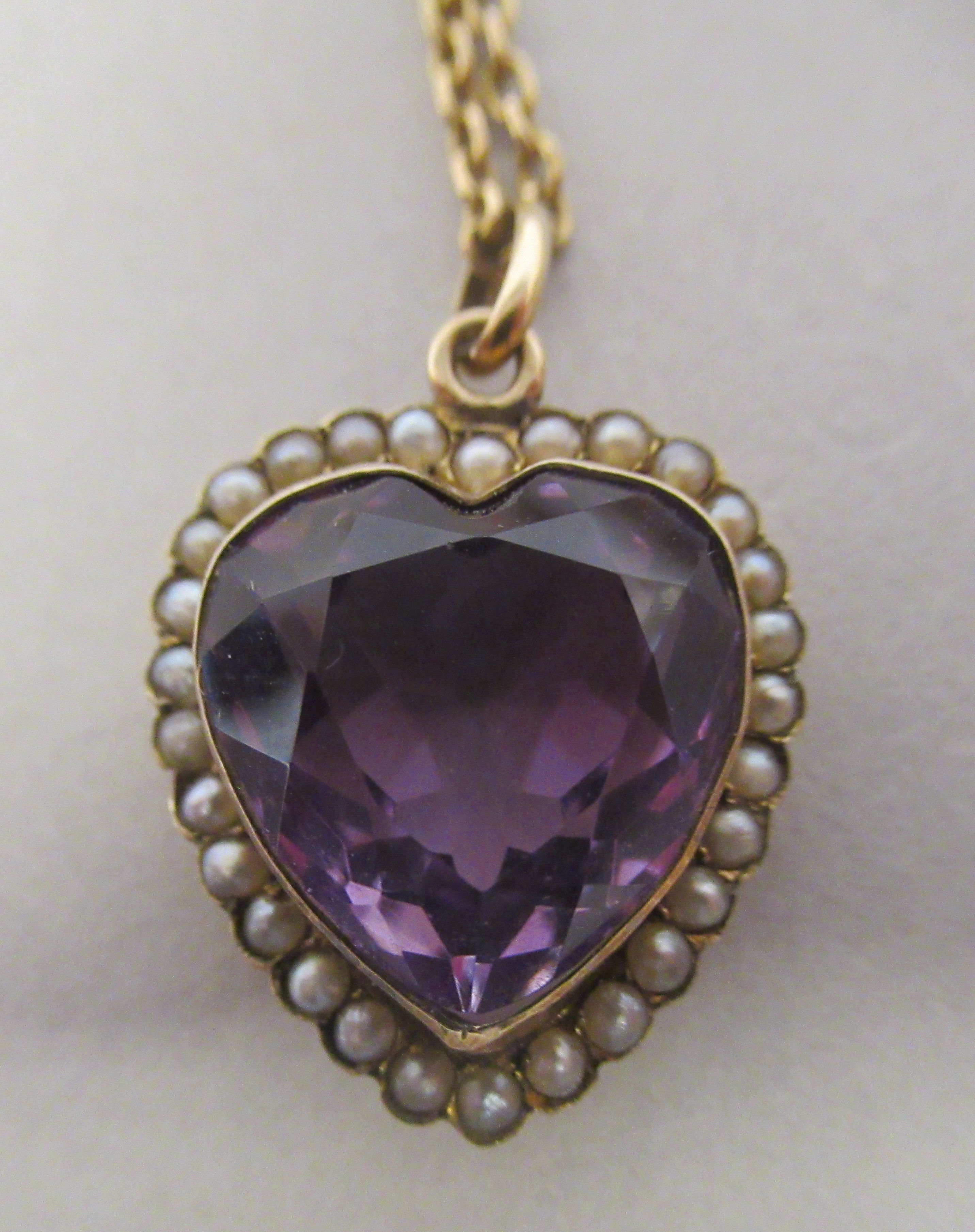 A 9ct gold heart shaped pendant, set with seed pearls around an amethyst coloured stone, on a fine