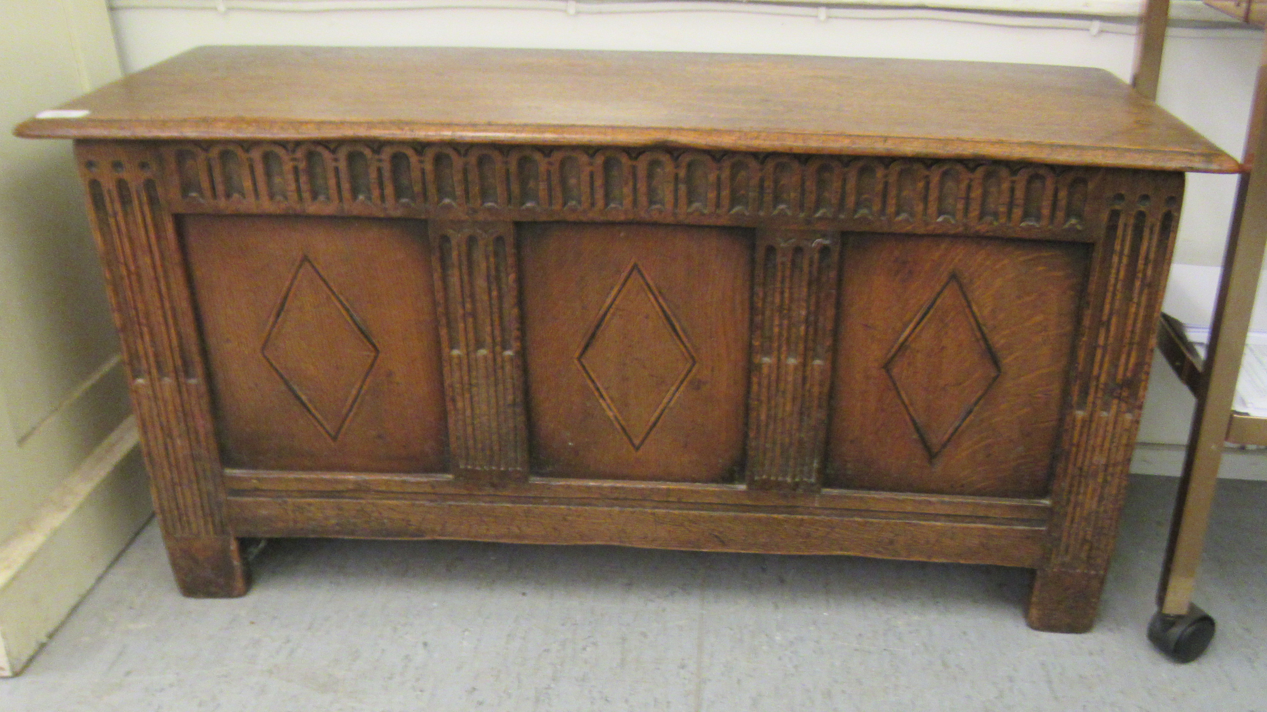 An early 20thC oak coffer with straight sides and a hinged lid, over a tri-panelled front, raised on