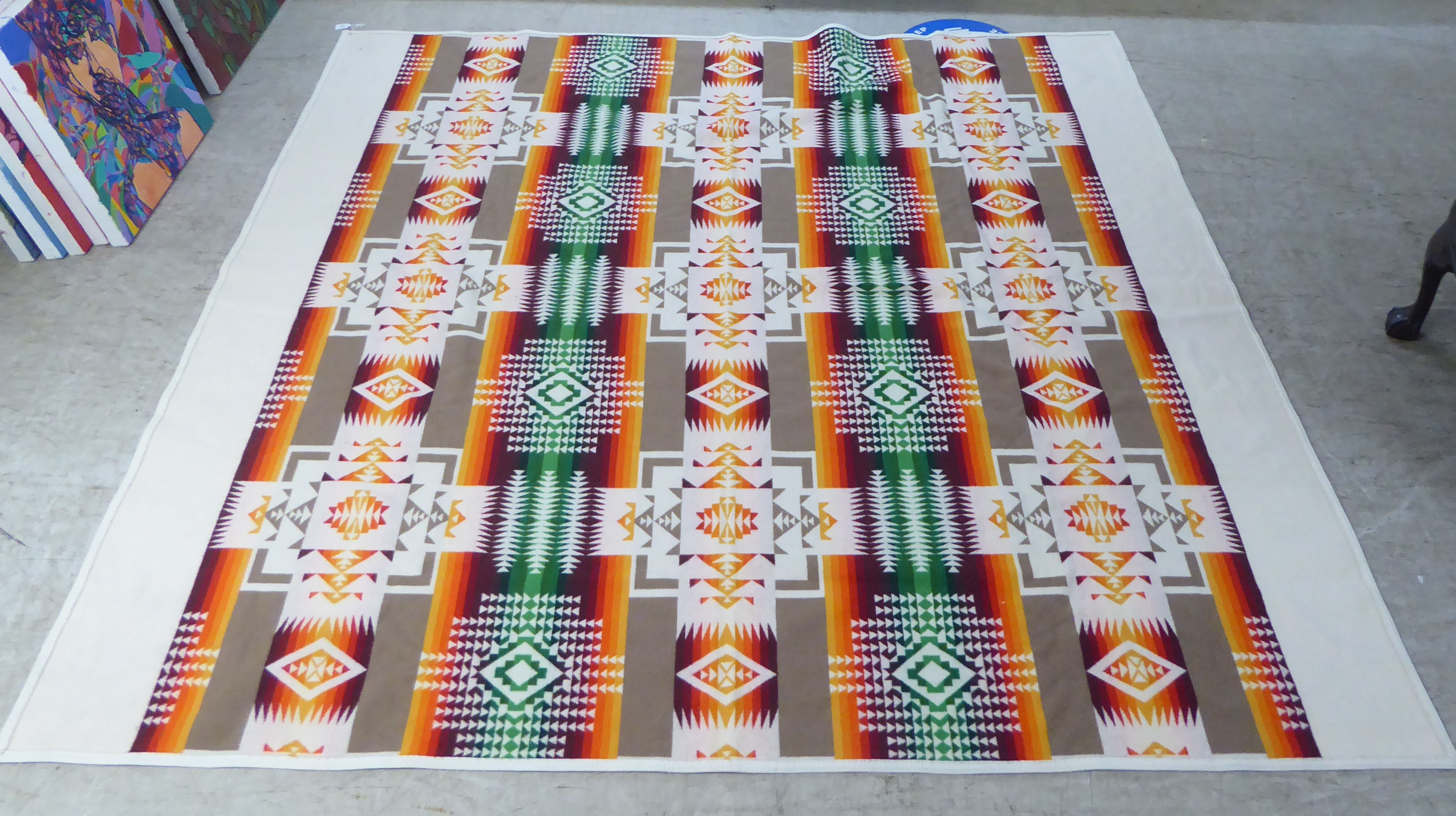 A Beaver State woollen throw/rug, highly decorated in orange and brown tones, on a cream coloured