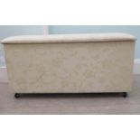 A modern cream coloured fabric upholstered ottoman with straight sides and a cushioned, hinged seat,