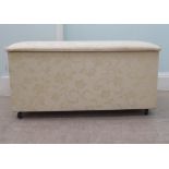 A modern cream coloured fabric upholstered ottoman with straight sides and a cushioned, hinged seat,