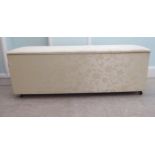 A modern cream coloured fabric upholstered ottoman with straight sides and a cushioned, hinged seat,
