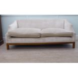 A modern three person settee with a level back and swept enclosed arms, upholstered in off white