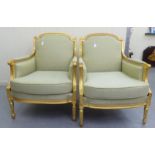 A pair of modern Louis XVI style antique finished gilded showwood framed enclosed arm salon chairs,