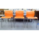 A set of three modern stacking chairs, each with a moulded orange plastic back and seat, raised on