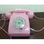 A pink plastic cased cradle type telephone handset with a rotating dial