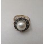 A yellow metal ring, set with a cultured pearl, surrounded by diamonds