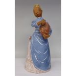 A Margit Kovacs art pottery standing figure wearing a blue pinafore dress, holding a loaf of bread