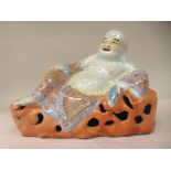 A 20thC Chinese porcelain figure, Buddha, the reclining deity holding a sack of coins, on a rocky