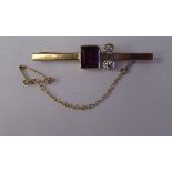 A 9ct gold bar brooch, on a safety chain, set with two diamonds and a ruby coloured stone