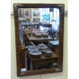 An early 20thC Chinese mirror, the plate set in a foliate and floral carved fruitwood frame with