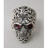 A silver coloured metal ring, featuring a skull with red glass eyes