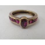 A gold coloured metal ring, set with a central ruby, flanked by ruby set shoulders  (stamped 14k)
