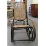 An early 20thC black painted bentwood framed rocking chair with a caned back and seat
