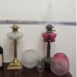 A late Victorian oil lamp with a cranberry coloured glass reservoir  16"h; and a later example, both