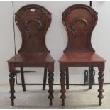 A pair of Regency mahogany hall chairs, each having a solid, waisted and foliate carved,