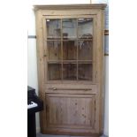 A late Victorian pine corner cabinet with a dentil moulded cornice, over an astragal glazed door,