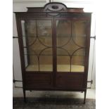 An Edwardian mahogany display cabinet with a carved upstand, over two astragal glazed doors,