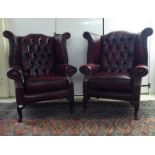 A pair of modern wingback armchairs, stud and part button upholstered in oxblood coloured hide,