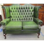 A modern wingback settee, stud and part button upholstered in green hide, raised on cabriole