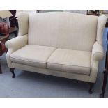 A modern two person wingback settee with enclosed arms, upholstered in cushioned biscuit coloured