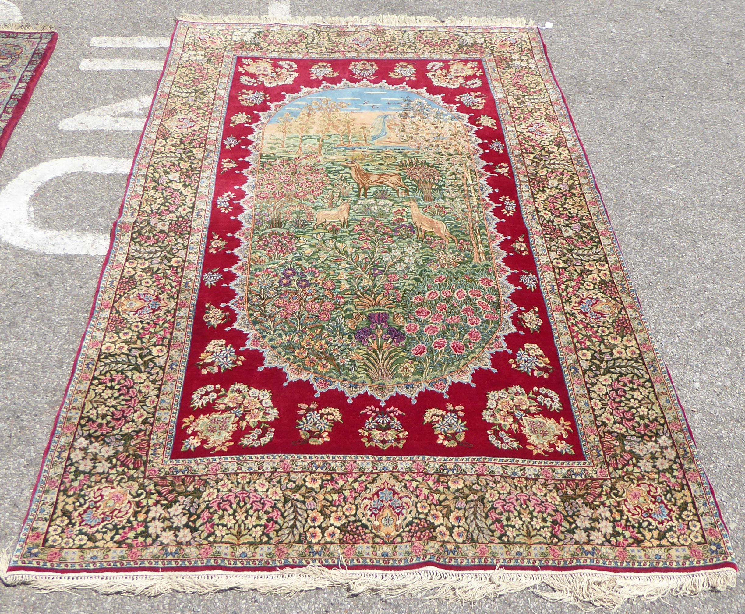 A Persian rug, decorated with pictorial cartouche, featuring deer in a woodland setting, bordered by