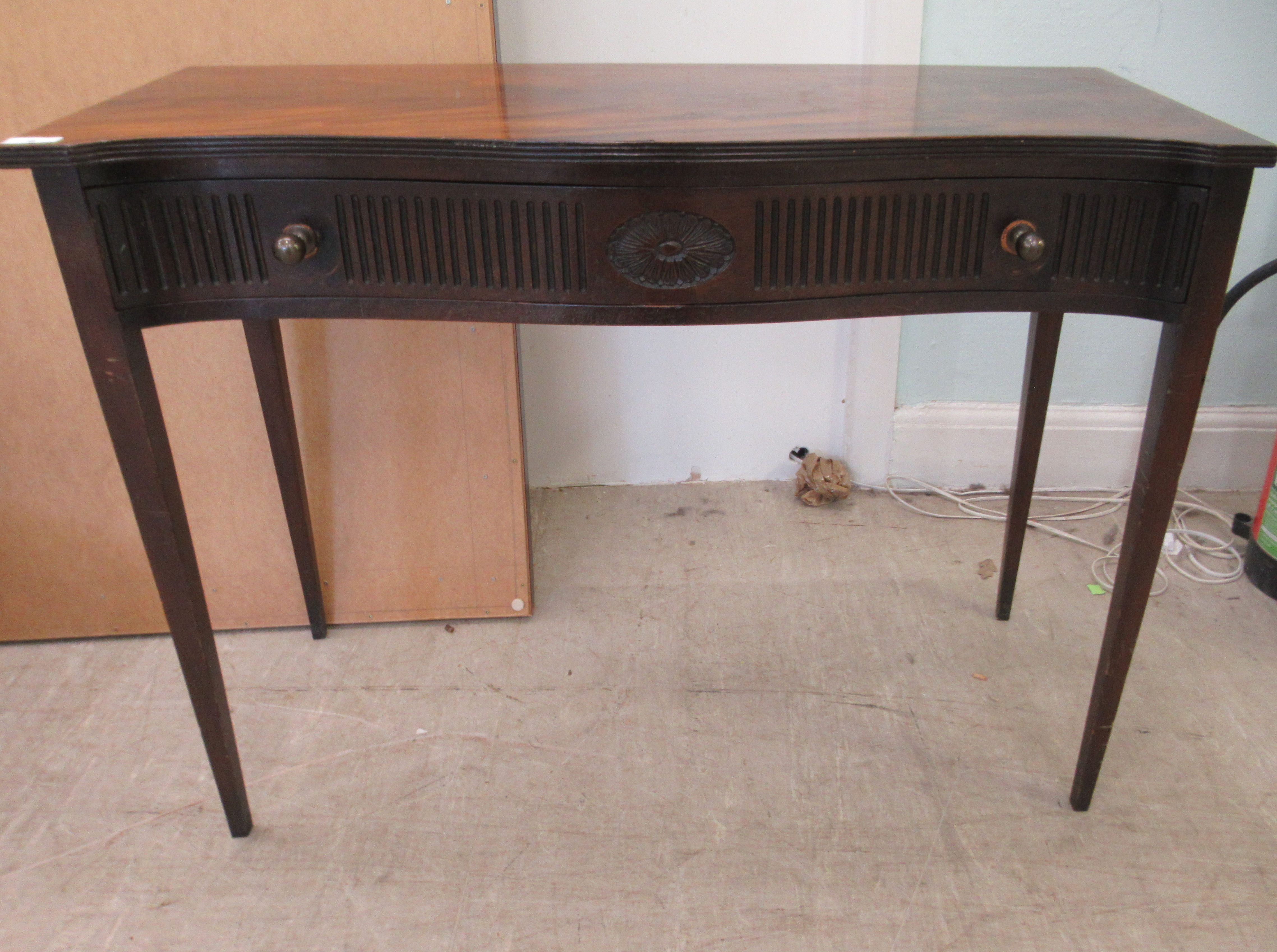 An early 20thC mahogany veneered serpentine front single drawer side table, raised on square,