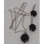 A 14k white gold earrings and pendant suite, set with a central black stone, surrounded by diamonds