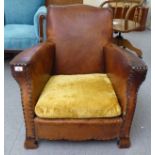 An early 20thC stud upholstered simulated tan/brown hide fireside chair, raised on block feet
