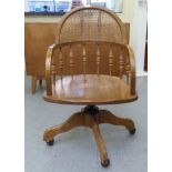 An early 20thC oak framed and woven cane backed office chair, raised on a quatrefoil base and