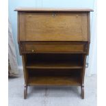 An early 20thC light oak student's bureau with a fall flap, over two open shelves, raised on planked