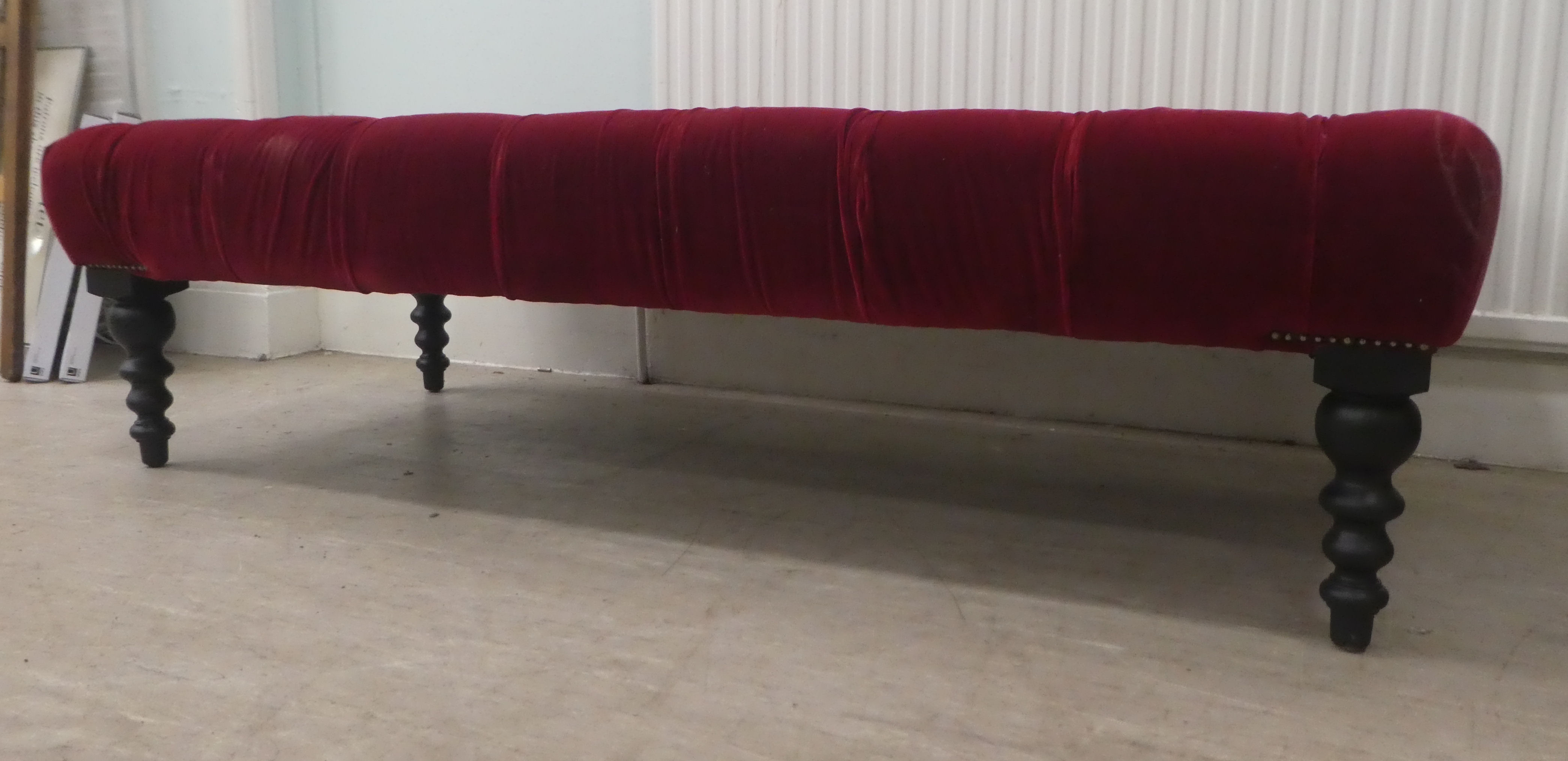 A modern footstool, part button upholstered in red fabric, over a stained wooden frame